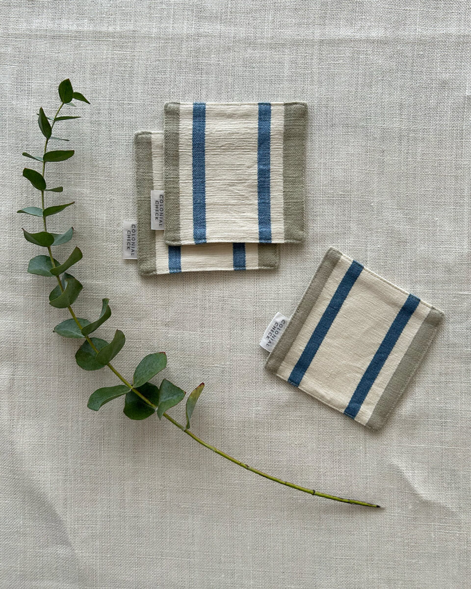 Beige linen napkins with blue vertical stripes laid on a light linen fabric, with a eucalyptus stem beside them.