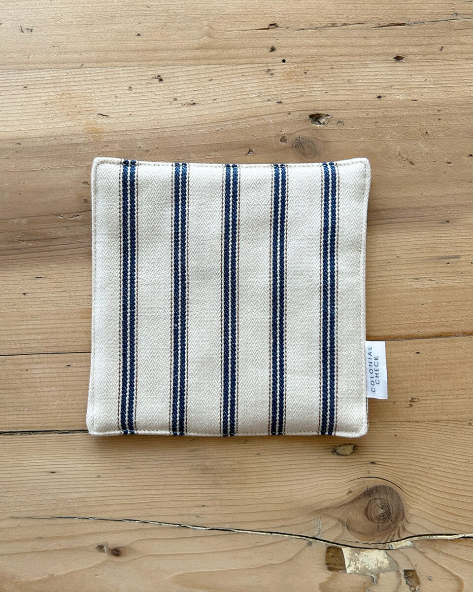 Cream-colored fabric pouch or napkin with bold blue vertical stripes on a wooden table surface, tag visible on the right edge.