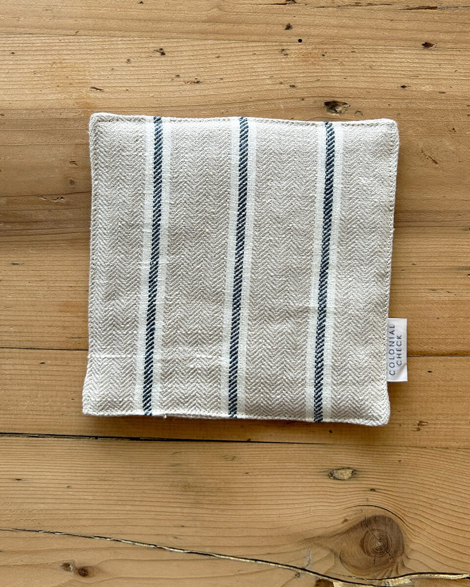 Folding white kitchen towel with blue stripes laid flat on a light wooden table.