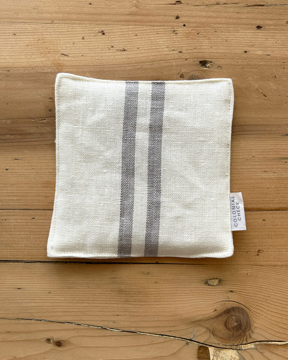 Beige fabric pouch with two vertical gray stripes on a wooden surface.