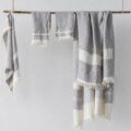 Gray and white striped towels or blankets draped over a wooden rod against a light wall, with fringed edges visible.