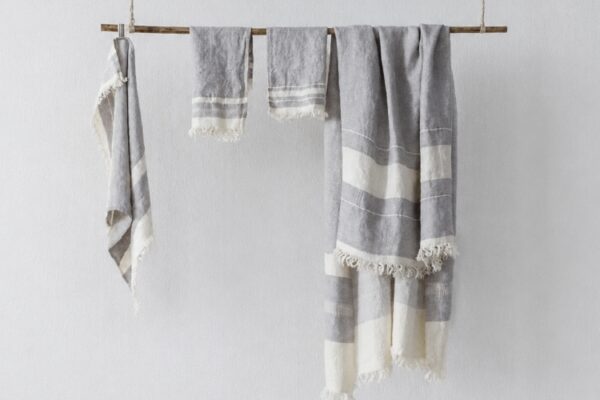 Gray and white striped towels or blankets draped over a wooden rod against a light wall, with fringed edges visible.