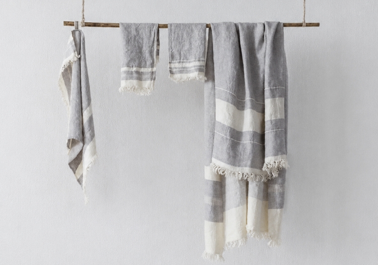 Gray and white striped towels or blankets draped over a wooden rod against a light wall, with fringed edges visible.