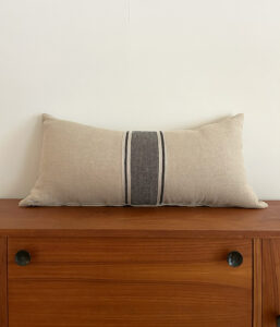 Beige rectangular decorative pillow with a dark gray central stripe resting on a wooden dresser against a white wall.