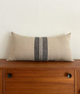 Beige rectangular decorative pillow with dark vertical stripe on a wooden dresser against a pale wall.