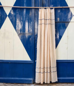 Beige striped curtain hanging from a rod in front of a glossy blue door with white geometric patterns in the background