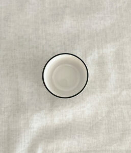 Top-down view of an empty white ceramic cup with a black rim on light gray fabric.