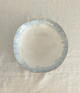 Top-down view of a round ceramic bowl with a pale blue glazed rim on a white tablecloth surface.