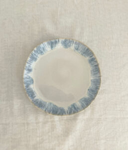 Round ceramic plate with a pale center and blue textured rim on a light fabric surface.