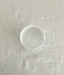 Top-down view of a white disposable cup with a small amount of clear liquid on a pale cloth table surface.