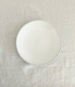 Top-down view of an empty white round plate on a pale linen surface.