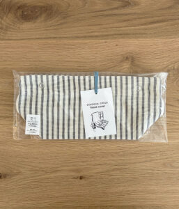 Colonial Check tissue cover in striped fabric, packaged in clear plastic on a wooden table with a price tag attached