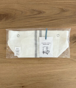 White fabric tissue cover with a gray central stripe, packaged in clear plastic with a tag that reads 'Colonial Check tissue cover'