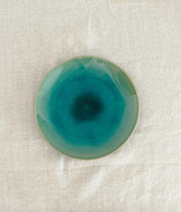 Round ceramic plate with a turquoise gradient glaze on a light fabric background