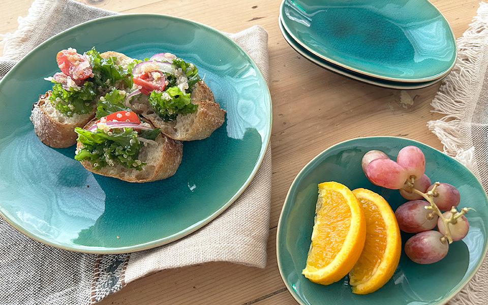 Crusty bread slices topped with greens, tomatoes, and cheese on a turquoise plate