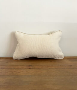Beige rectangular throw pillow on a wooden surface against a light wall.