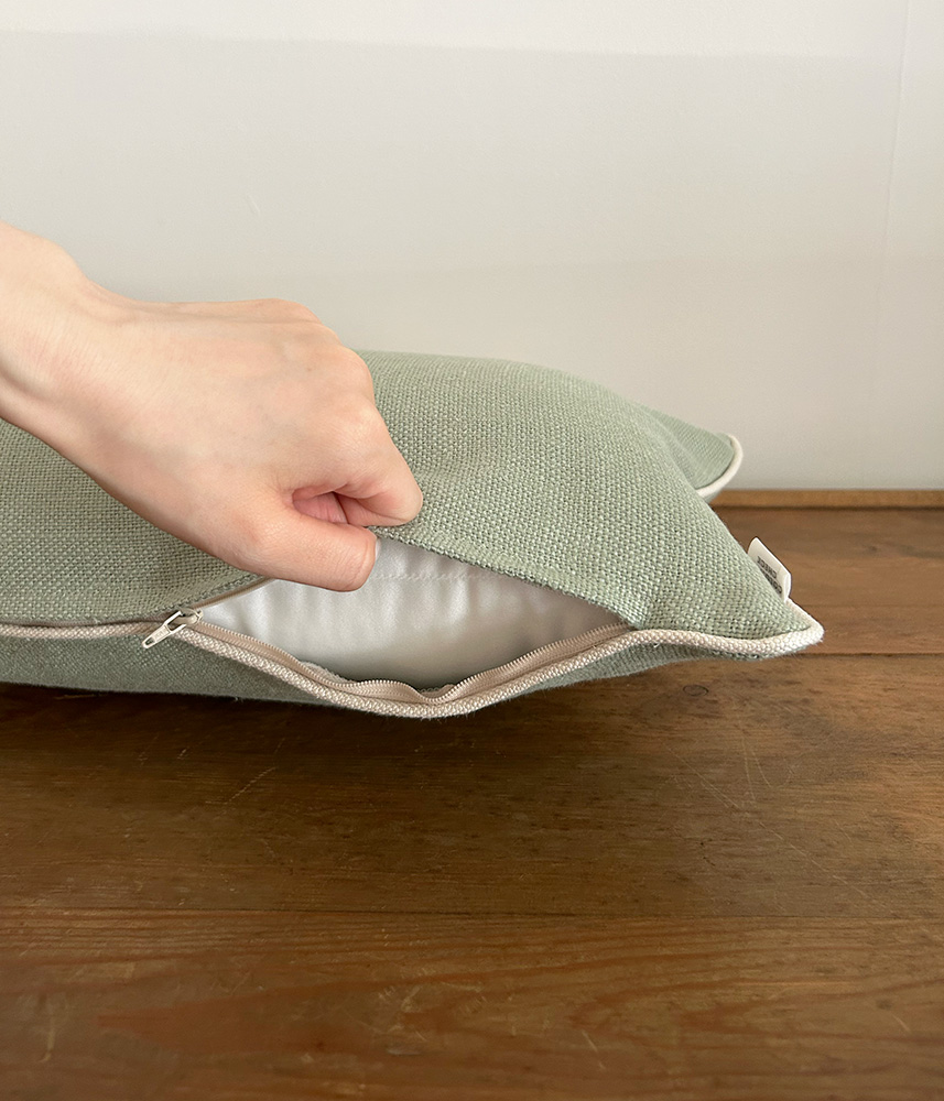 Person lifting the zipper on a light green cushion to reveal the white inner lining inside a wooden tabletop setting.