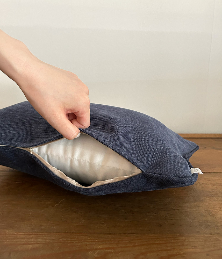 Hand pulling back the zipper of a navy blue fabric cushion to reveal a white inner lining on a wooden surface.
